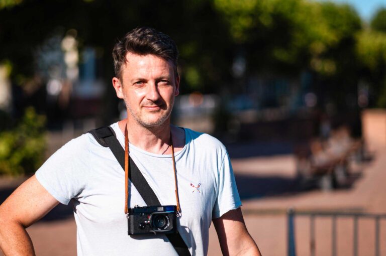 Porträt eines Fotografen mit Kamera um den Hals, aufgenommen im Sonnenlicht – Spezialist für Landschafts-, Reise-, Streetfotografie und Blog.