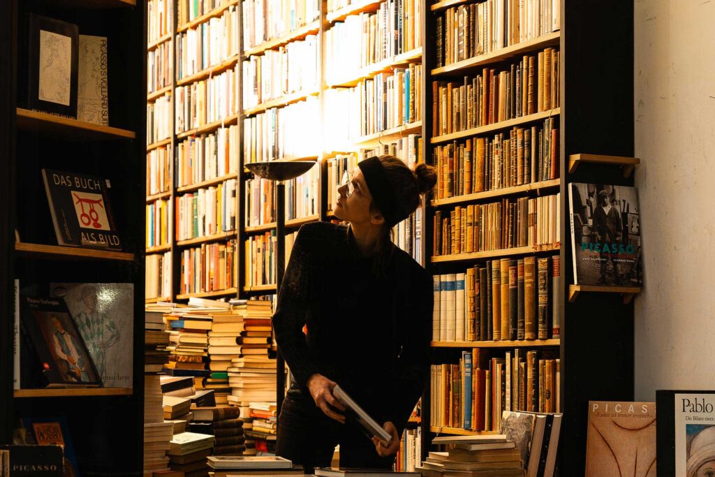 Frau in einem Heidelberger Antiquariat zwischen hohen Bücherregalen im warmen Licht einer Lampe