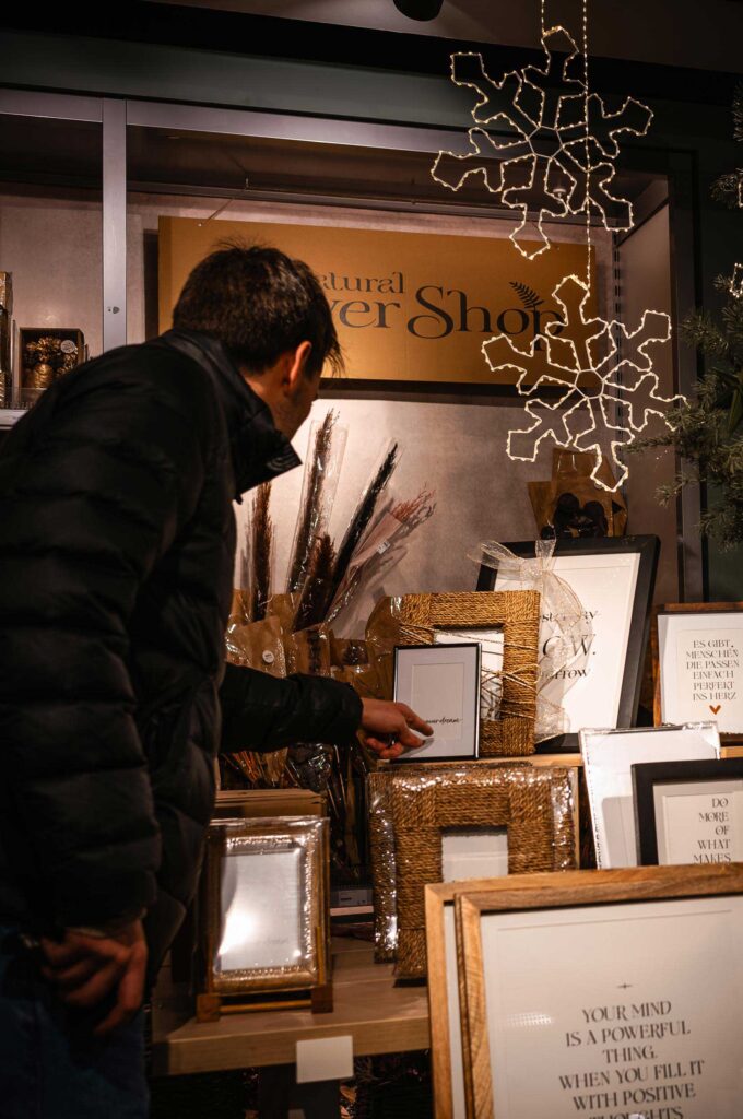 Mann betrachtet Bilderrahmen in weihnachtlich dekoriertem Concept Store mit Lichterketten und Schneeflocken