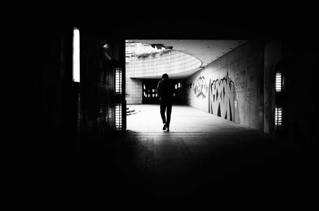 Silhouette einer Person läuft durch einen dunklen Tunnel in Wien in Richtung Licht, Schwarzweißaufnahme mit starkem Kontrast und urbaner Graffiti-Umgebung.